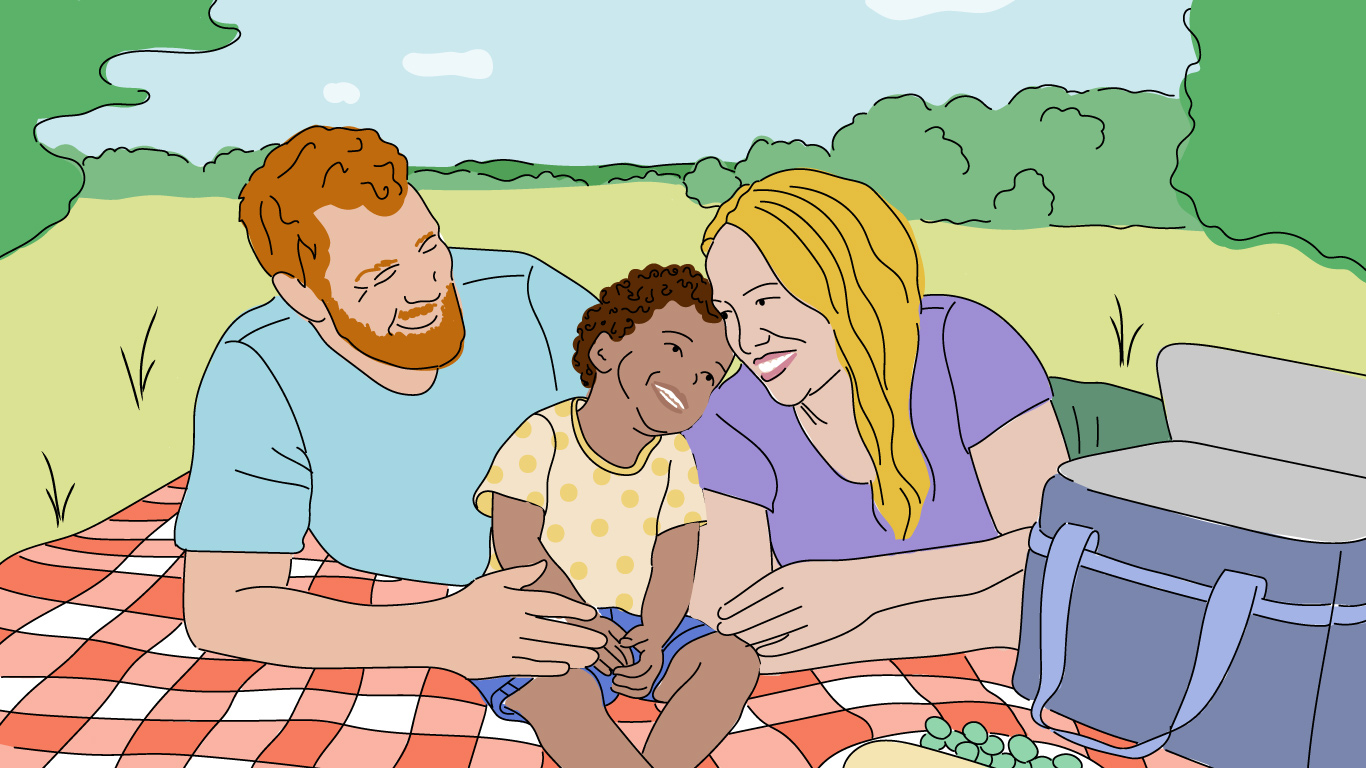 Ein Elternpaar sitzt mit einem Kind auf einer Picknickdecke auf einer Wiese